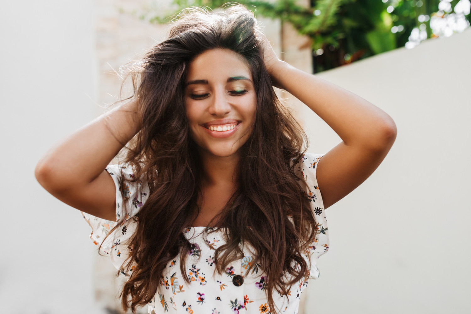 attractive tanned woman white blouse with charming smile posing white wall with green plants